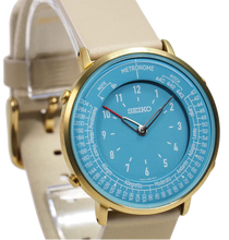 Seiko Metronome Watch SMW005A side view with golden case, sky‑blue dial, khaki leather strap, dual‑function time and tempo display.